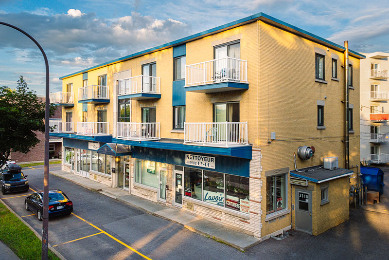 Le Parisien : immeuble jaune de trois étages avec balcons blancs, commerces au rez-de-chaussée sur le boulevard Sainte-Anne.