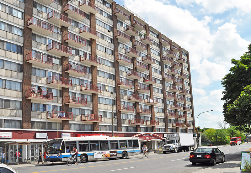 Place Sutton, rue Sherbrooke Ouest : tour de logements en brique avec balcons, commerces au rez-de-chaussée.