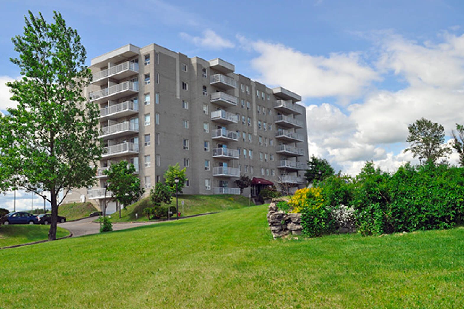 Un complexe résidentiel du Groupe Laberge, sept étages avec balcons, pelouse et arbres en été